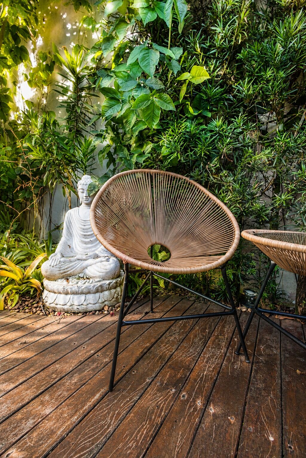 A wicker chair with a circular seat and backrest, positioned on a wooden deck.