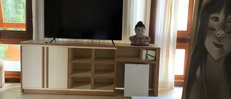Una sala de estar con un televisor de pantalla plana, una lámpara de mimbre, una pequeña estatua y un cuadro en un tablero de madera.
