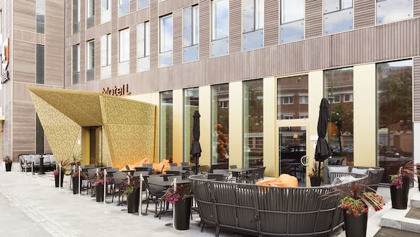Un espace extérieur aménagé avec des tables et des chaises, une grande structure décorative et un bâtiment sur lequel on peut lire l’inscription « Motel ».