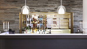Un espace bar avec un mur en pierre en arrière-plan, deux suspensions lumineuses et une variété de bouteilles et de verres exposés.