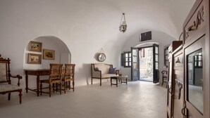 A spacious room with a high ceiling, a dining area with wooden furniture, a sofa with a cushion, and a large mirror. - Casa Santantonio (Santorini)