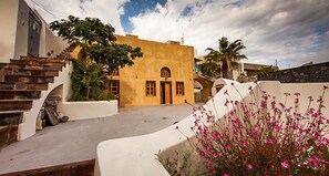 A traditional building with a yellow facade, a staircase, and a garden with pink flowers. - Casa Santantonio (Santorini)