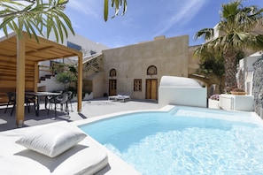 A pool area with a pergola, lounge chairs, and a dining set. - Casa Santantonio (Santorini)