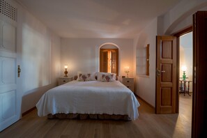 A bedroom with a large bed, two bedside tables with lamps, a wooden door, and a small table with a lamp in the corner. - Casa Santantonio (Santorini)