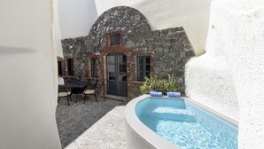 A stone building with a pool, a table with chairs, and a door. - Casa Santantonio (Santorini)