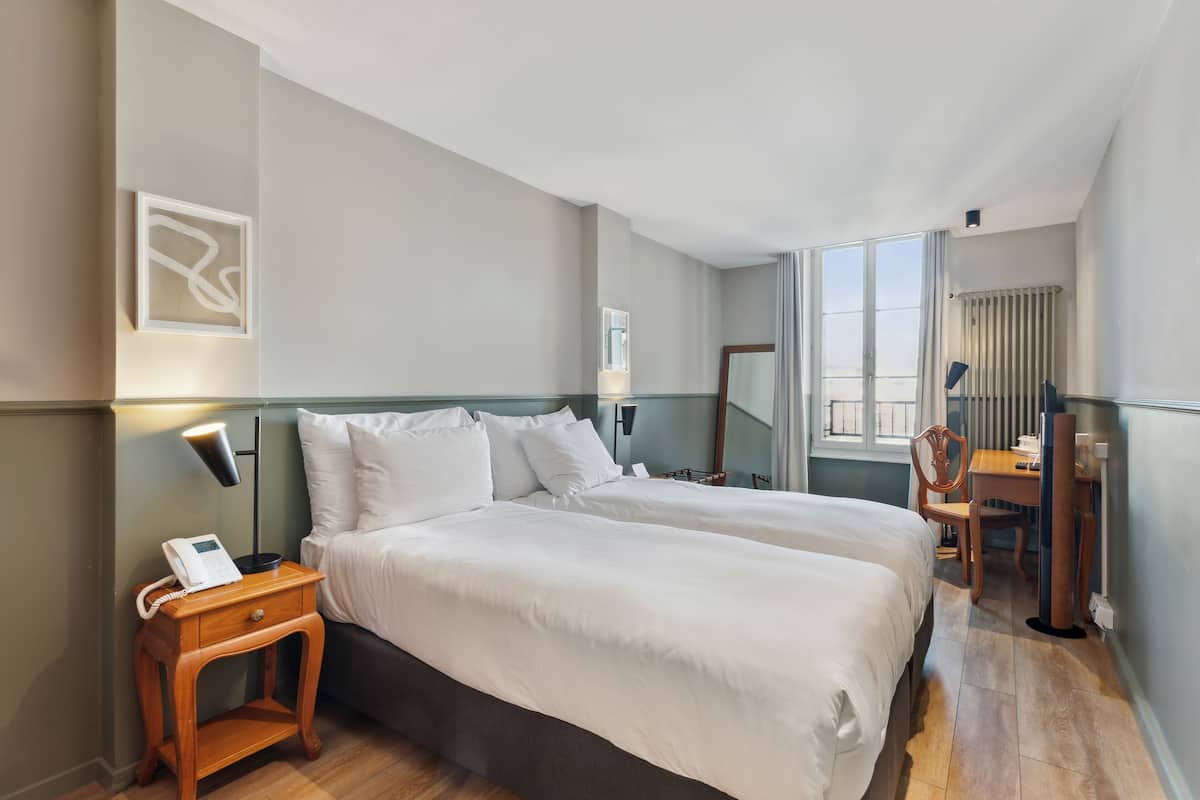 Een hotelkamer met twee bedden, een bureau, een stoel, een lamp en een telefoon op een nachtkastje.