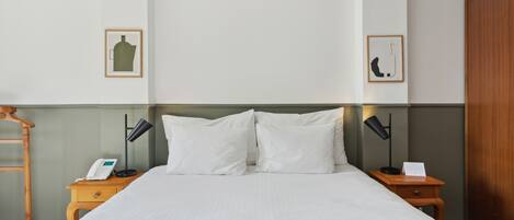 Una cama bien hecha con sábanas blancas, dos mesitas de noche con lámparas, una escalera de madera y cuadros en las paredes.