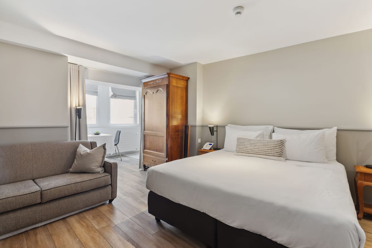 Een hotelkamer met een bed, een bank, een kledingkast en een bureau met een lamp.