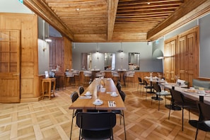 A spacious dining area with wooden tables and chairs, a long counter, and wooden cabinets. - Hôtel de la Couronne (Morges)