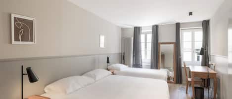 A hotel room with two beds, a desk, a chair, a lamp, a framed picture on the wall, and a window with curtains.