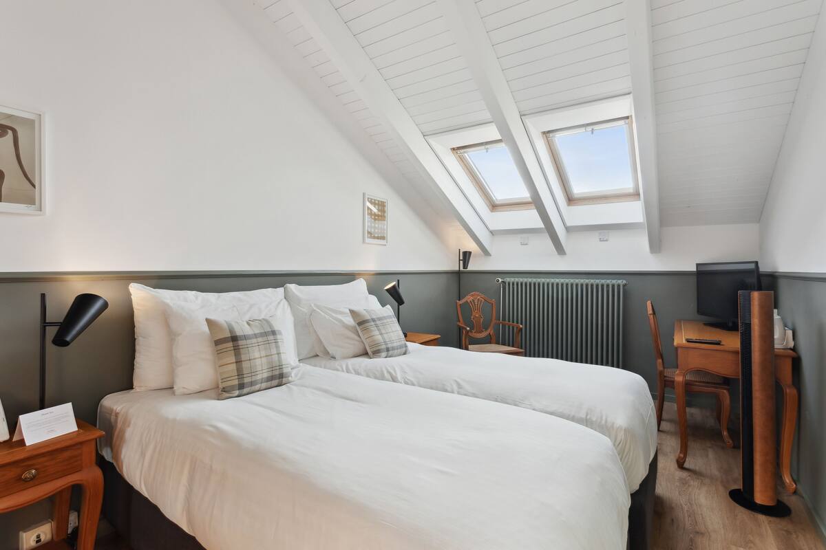 Een hotelkamer met twee bedden, een bureau, een stoel, een televisie en dakramen.