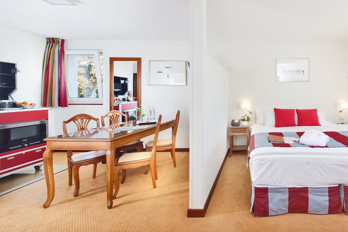 Une chambre d’hôtel comprenant un lit, une table de chevet, une lampe et un coin repas avec une table et des chaises.