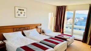 Habitación de hotel con dos camas, un cabecero de madera, un cuadro enmarcado en la pared y vistas a la ciudad a través de la ventana.