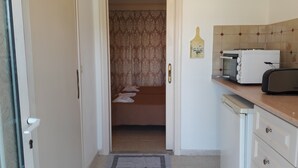 Una pequeña cocina con tostadora, microondas y pileta. Se observa una puerta que da a un cuarto con cama y cortina.