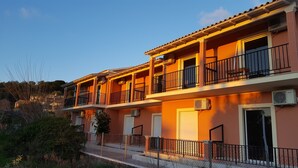 Un edificio de varios pisos con balcones, unidades de aire acondicionado y una cerca de malla metálica.