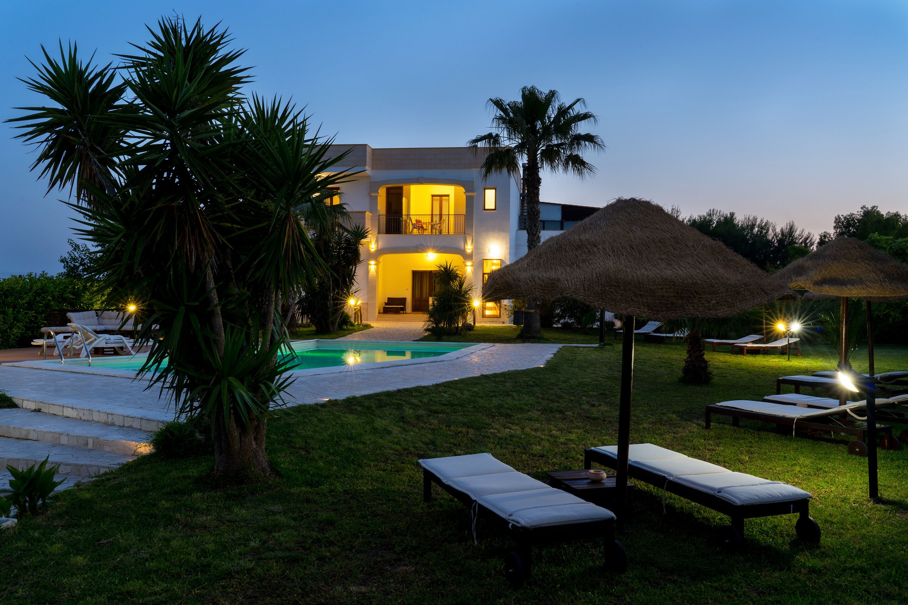 A modern villa with a swimming pool, lounge chairs, and thatched umbrellas.