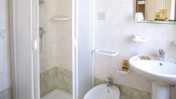 A bathroom with a shower, bidet, sink, and toilet.
