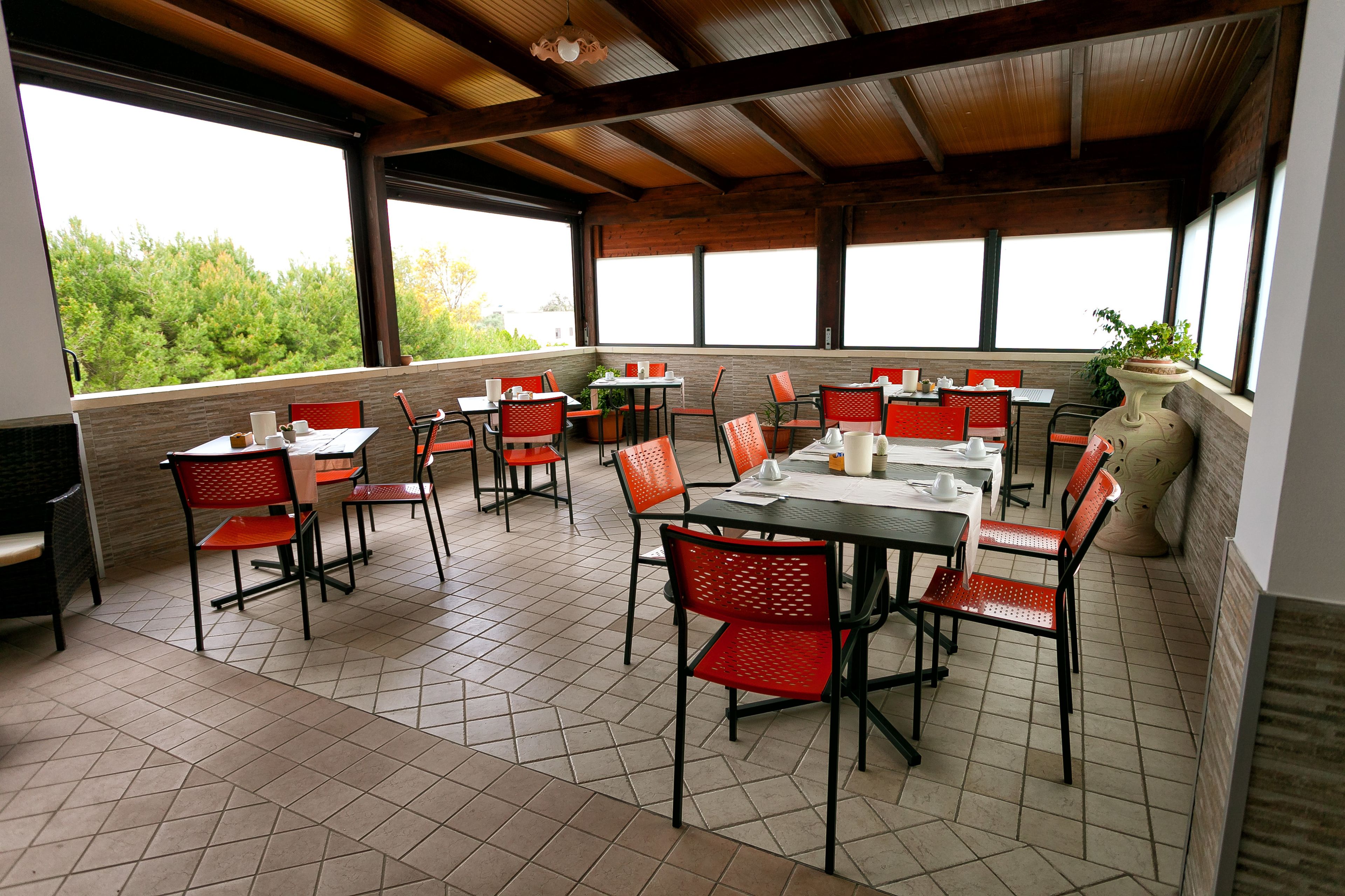 A restaurant with outdoor seating, multiple tables and chairs, and large windows offering views of greenery.