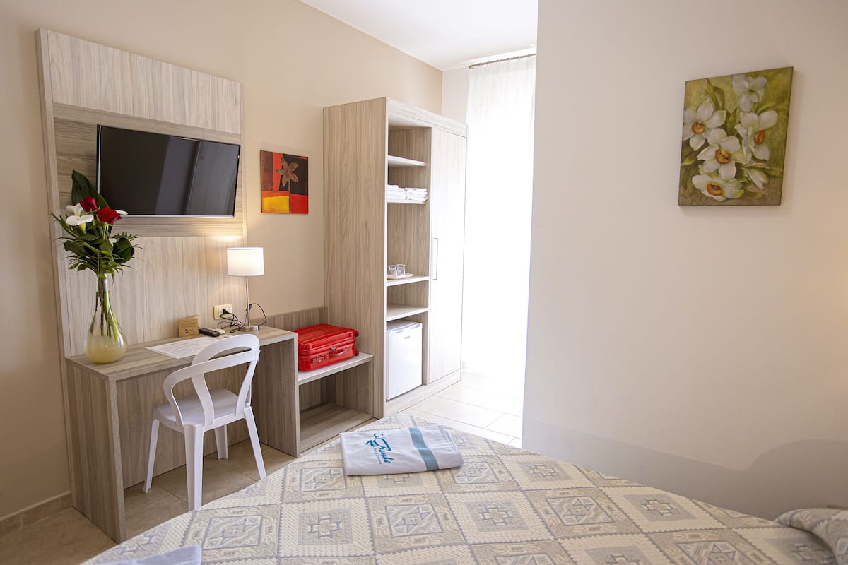 A hotel room with a bed, a desk with a chair, a TV, a wardrobe, and a painting on the wall.