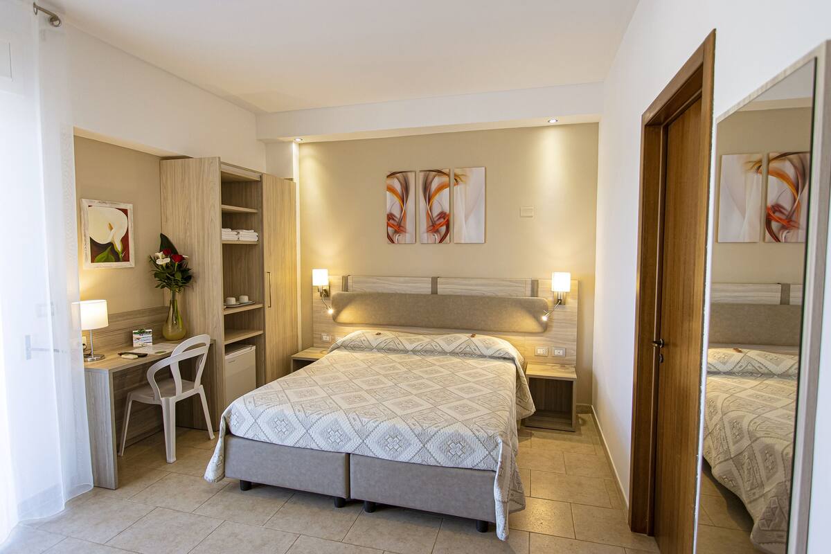 A hotel room with a bed, a desk, a chair, and a wardrobe.