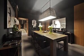 A modern kitchen with a wooden table, black chairs, and white orchids. There are framed pictures on the wall and a large pendant light above the table. - Parioli Place (Rome)