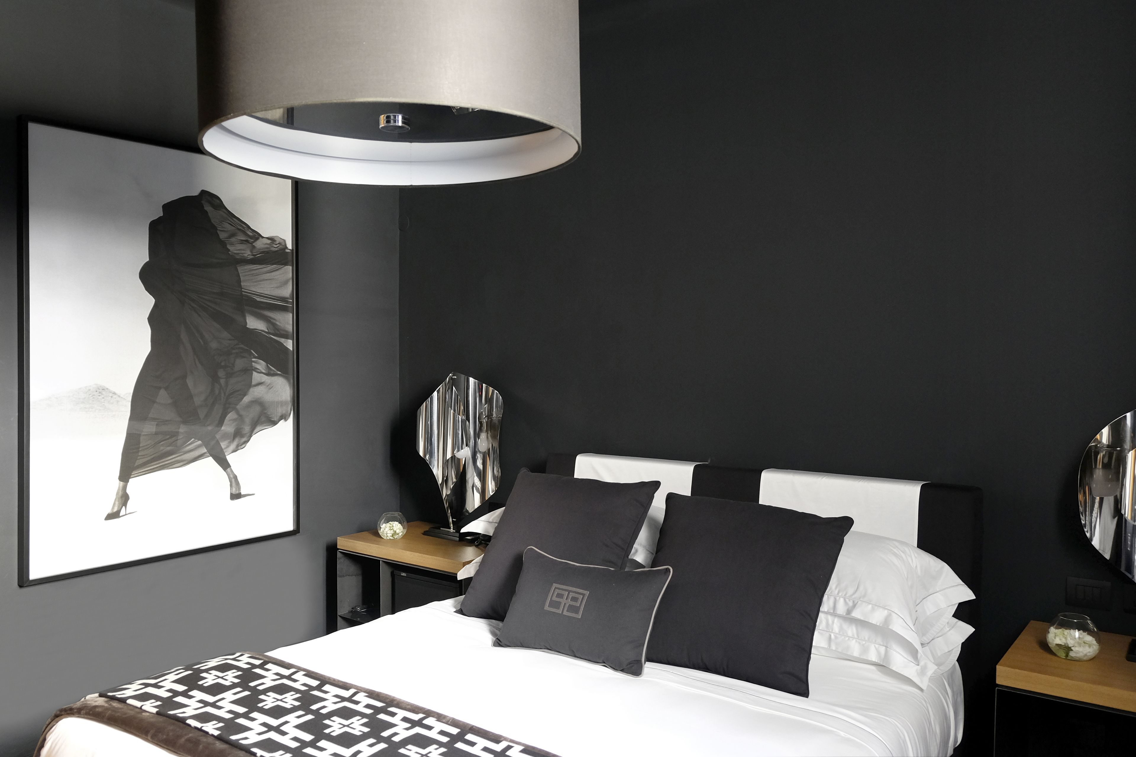 A modern bedroom with a large bed, a bedside table, a mirror, and a wall-mounted lamp.