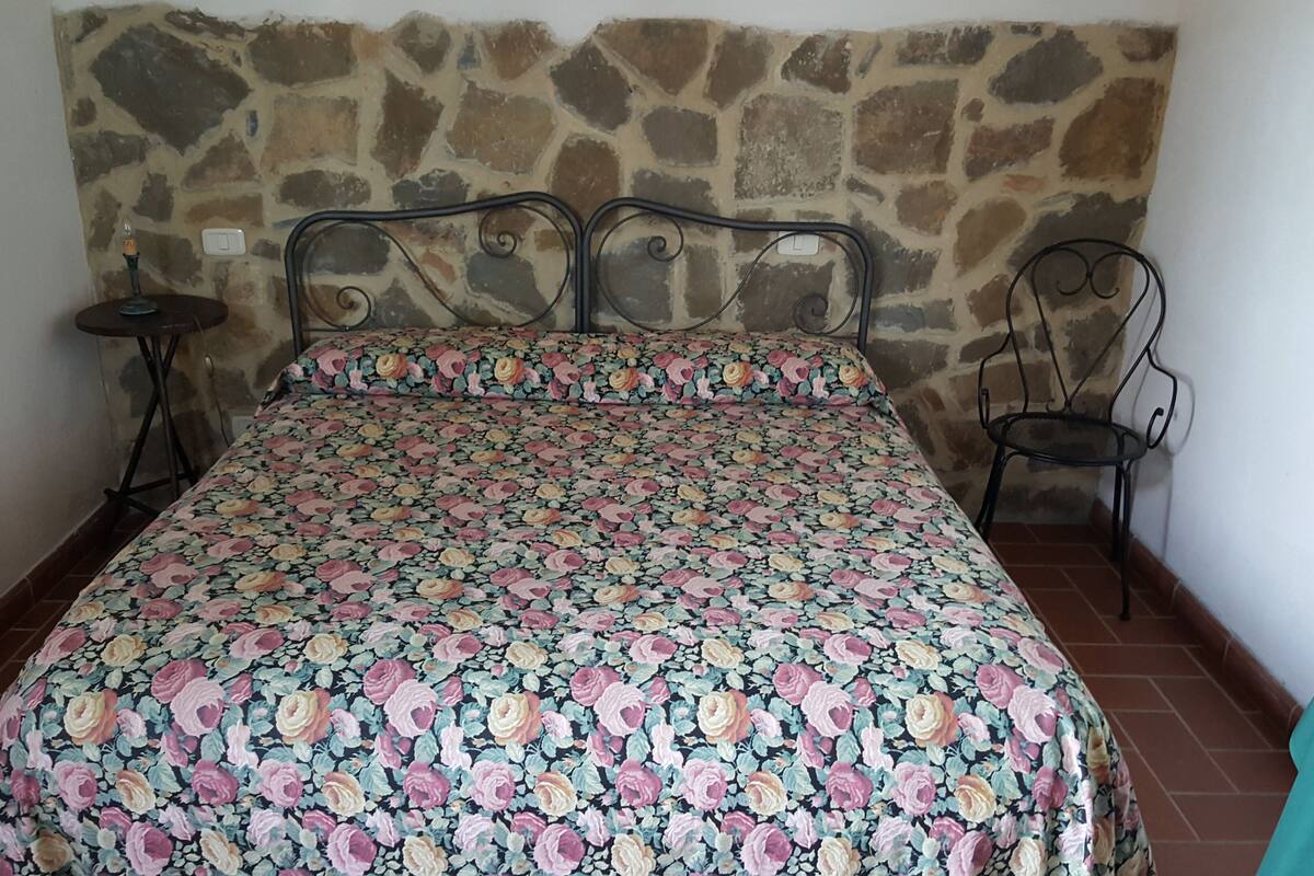 A bed with a floral bedspread, a stone wall, and a chair.