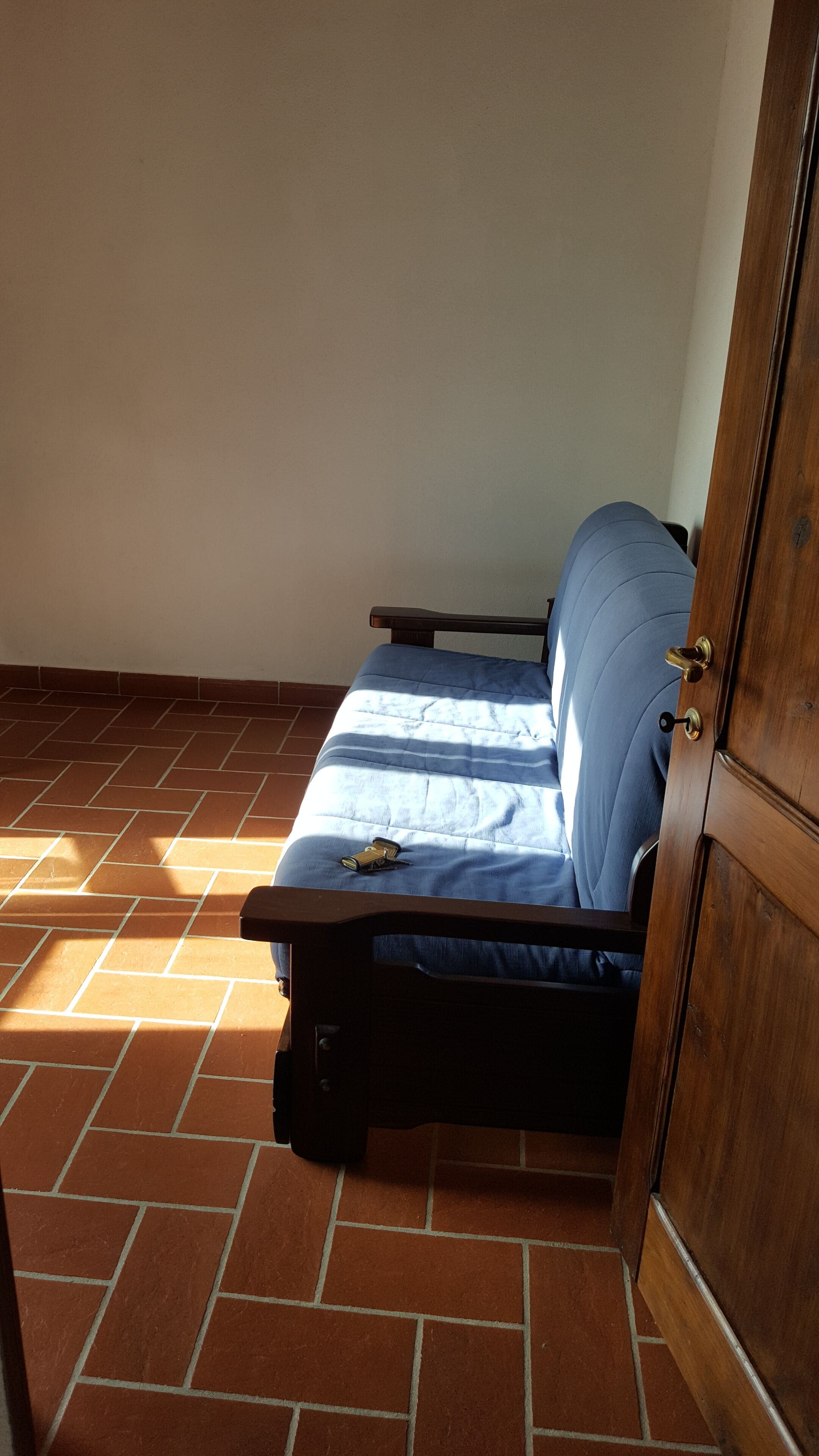 Una habitación pequeña con un sofá azul apoyado en una pared, un armario de madera y suelo de baldosas.