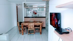 Eine moderne Küche mit weißen Schränken, einem Holzesstisch und einem Fernseher auf einem Holzschrank.