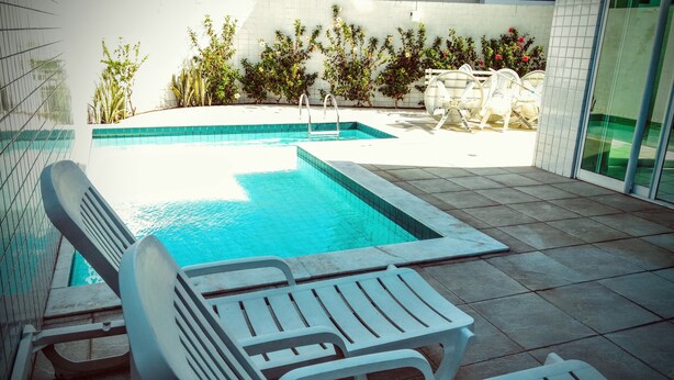 Ein Schwimmbecken mit Fliesenverkleidung, umgeben von Topfpflanzen und Gartenmöbeln.