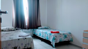 Een kamer met twee bedden, waarvan er één een bloemenlaken heeft en de ander een blauw bloemenlaken. Tussen de bedden hangt een verwarming aan de muur, en op het bed met het blauwe bloemenlaken ligt een rood object.