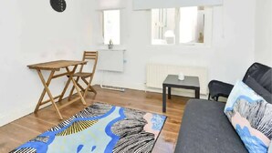 Ein kleiner, heller Raum mit einem Holztisch und Stühlen, einem Sofa und einem gemusterten Teppich.