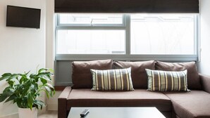 Ein modernes Wohnzimmer mit einem braunen Sofa, gestreiften Kissen, einer Topfpflanze und einer Fernbedienung auf einem Couchtisch.