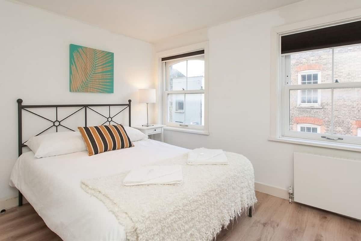 A bedroom with a bed, a window, a radiator, and a wall art piece.