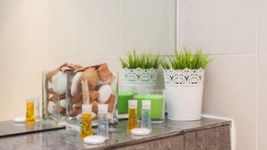 Ein Badezimmer-Waschtisch mit einem Glasbehälter voller Pflegeprodukten, einer Topfpflanze und mehreren Seifenflaschen.