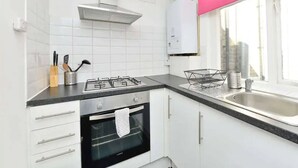 Eine moderne Küche mit weißen Schränken, einer schwarzen Arbeitsplatte, einem Edelstahlherd und einem Fenster mit rosa Rahmen.