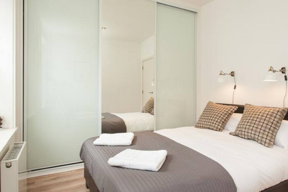 A modern hotel room with a large bed, two bedside lamps, and a mirror.