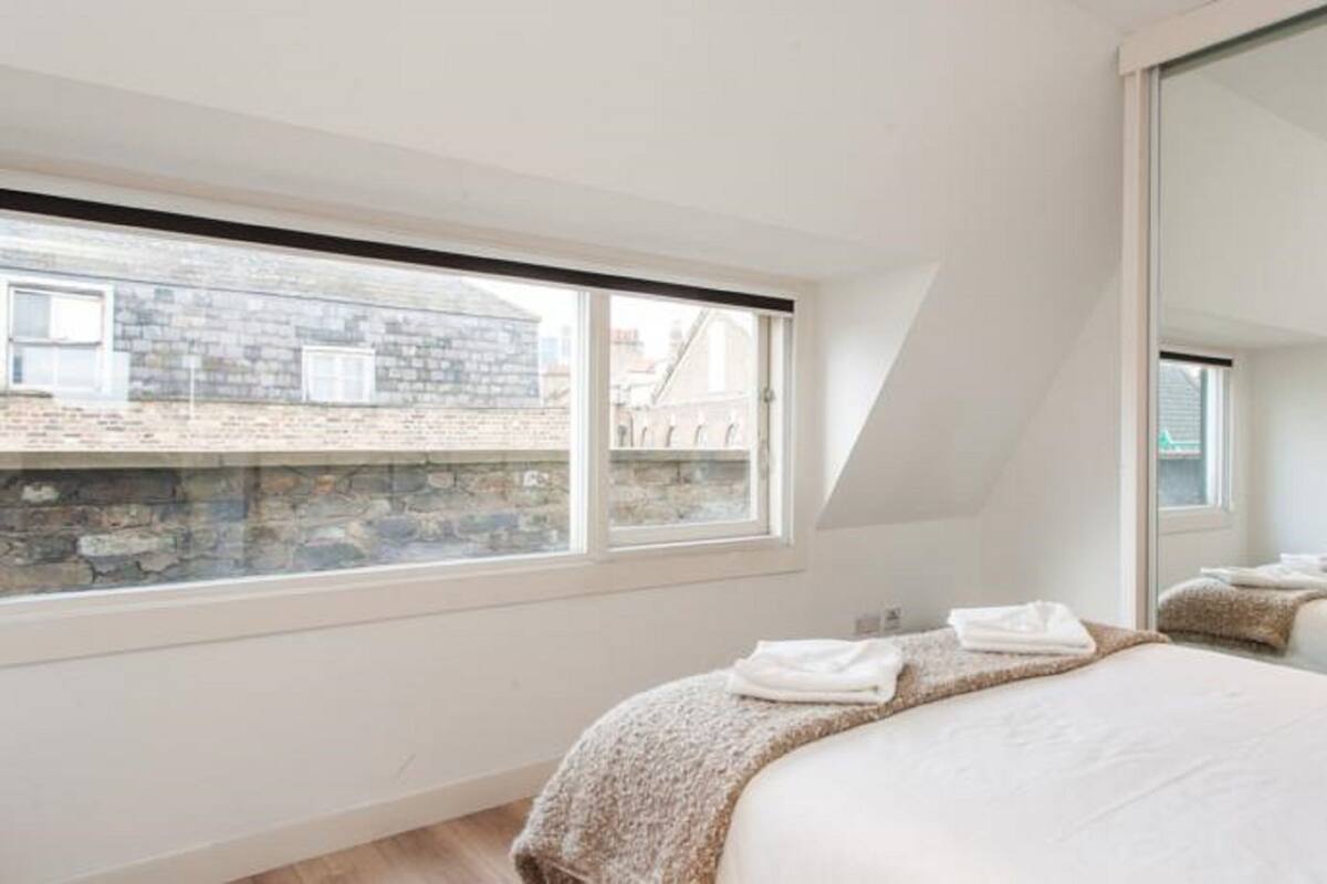 A bedroom with a large window, a bed with a blanket, and a mirror.