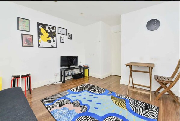 A living room with a flat-screen TV, a zebra-patterned rug, and a wooden table.