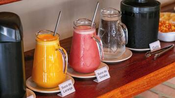 Bancada de buffet com diversos sucos de frutas e uma máquina de café.