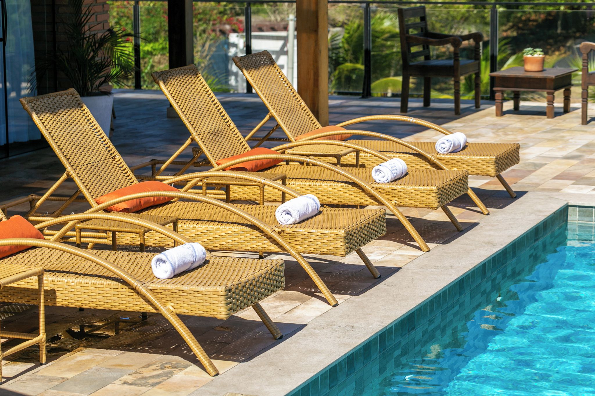 Área ao lado da piscina com espreguiçadeiras de vime e piscina revestida com azulejos.