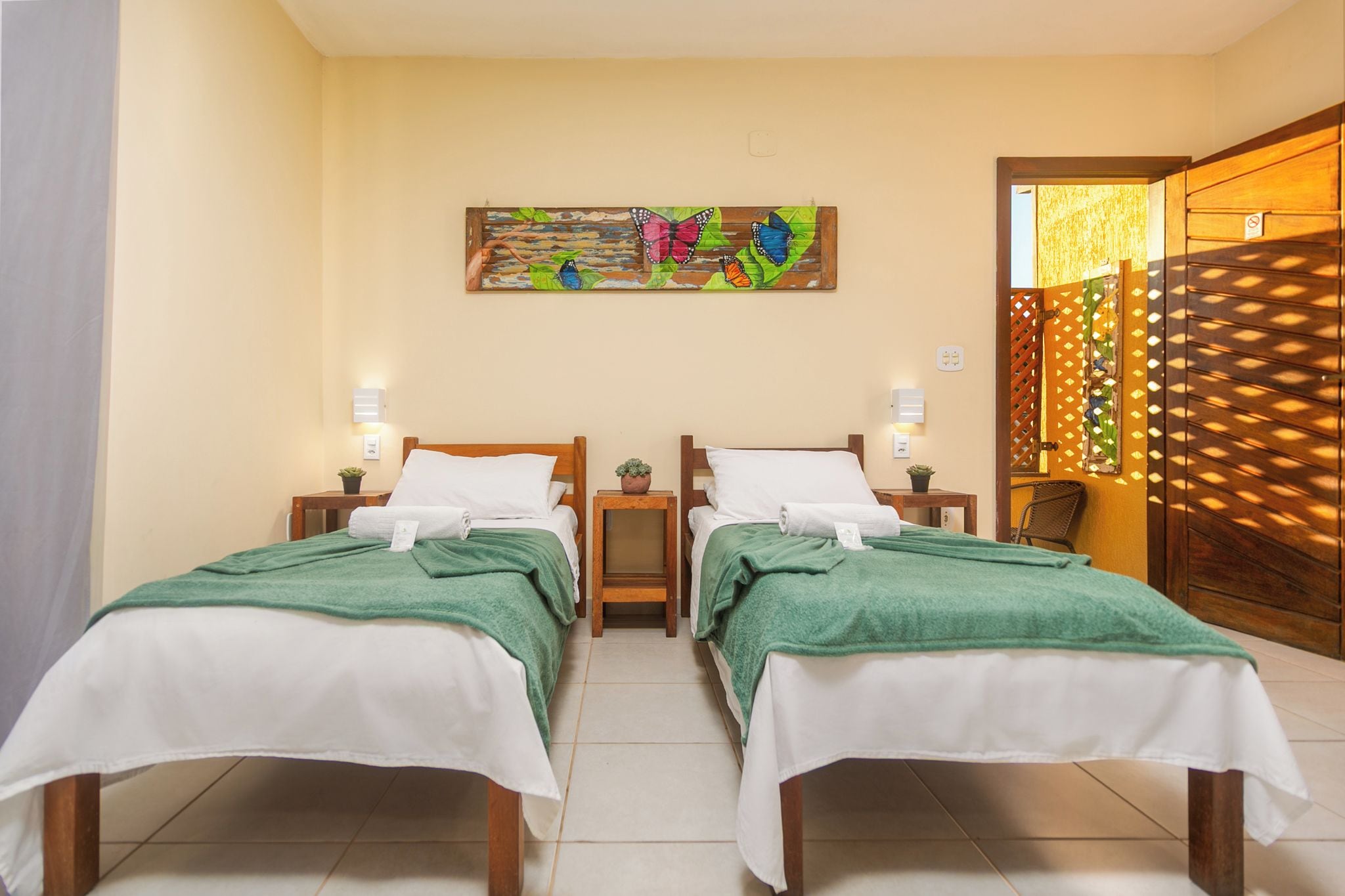 Habitación de hotel con dos camas individuales, una mesita pequeña, un cuadro colgado en la pared y una puerta de madera con diseño de celosía.
