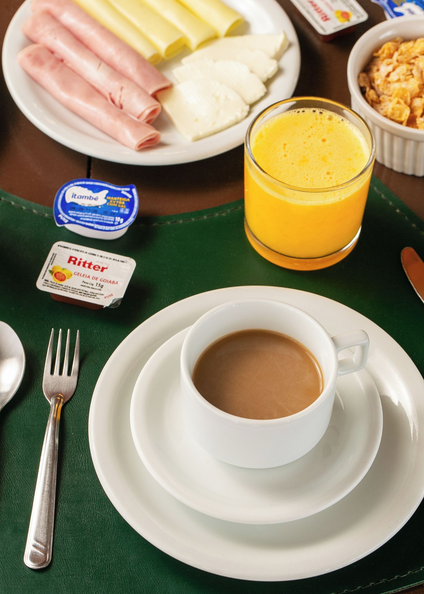 A breakfast setting with a plate of ham, cheese, and rolls, a glass of orange juice, a cup of coffee, and condiments.