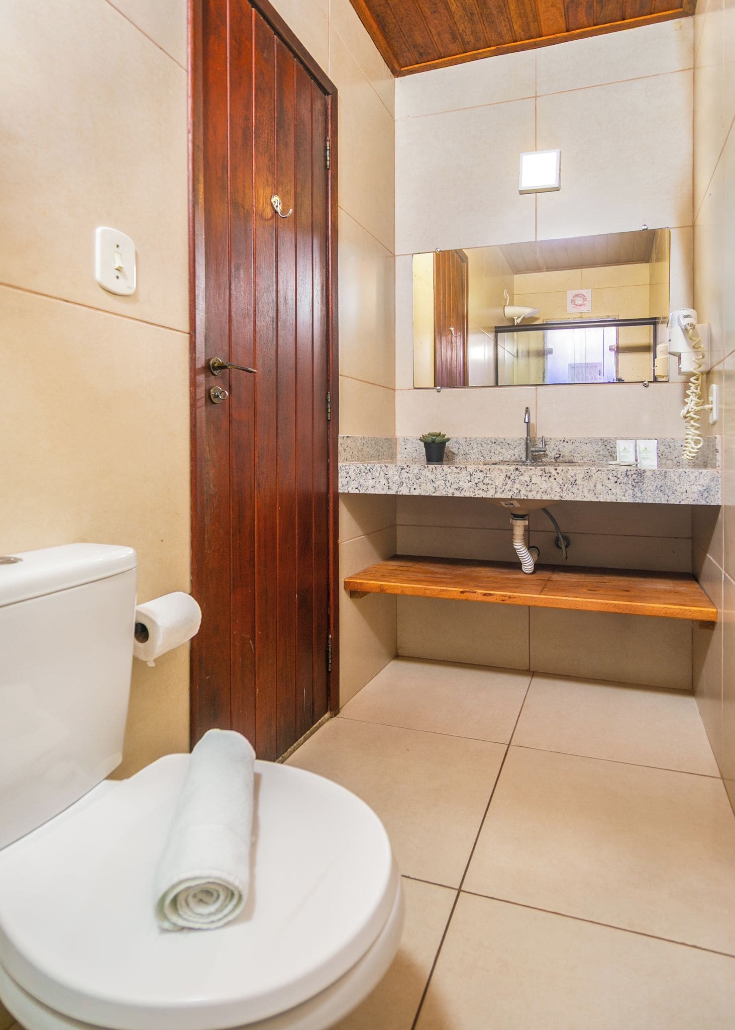 A bathroom with a toilet, a wooden door, a sink with a mirror, and a towel.