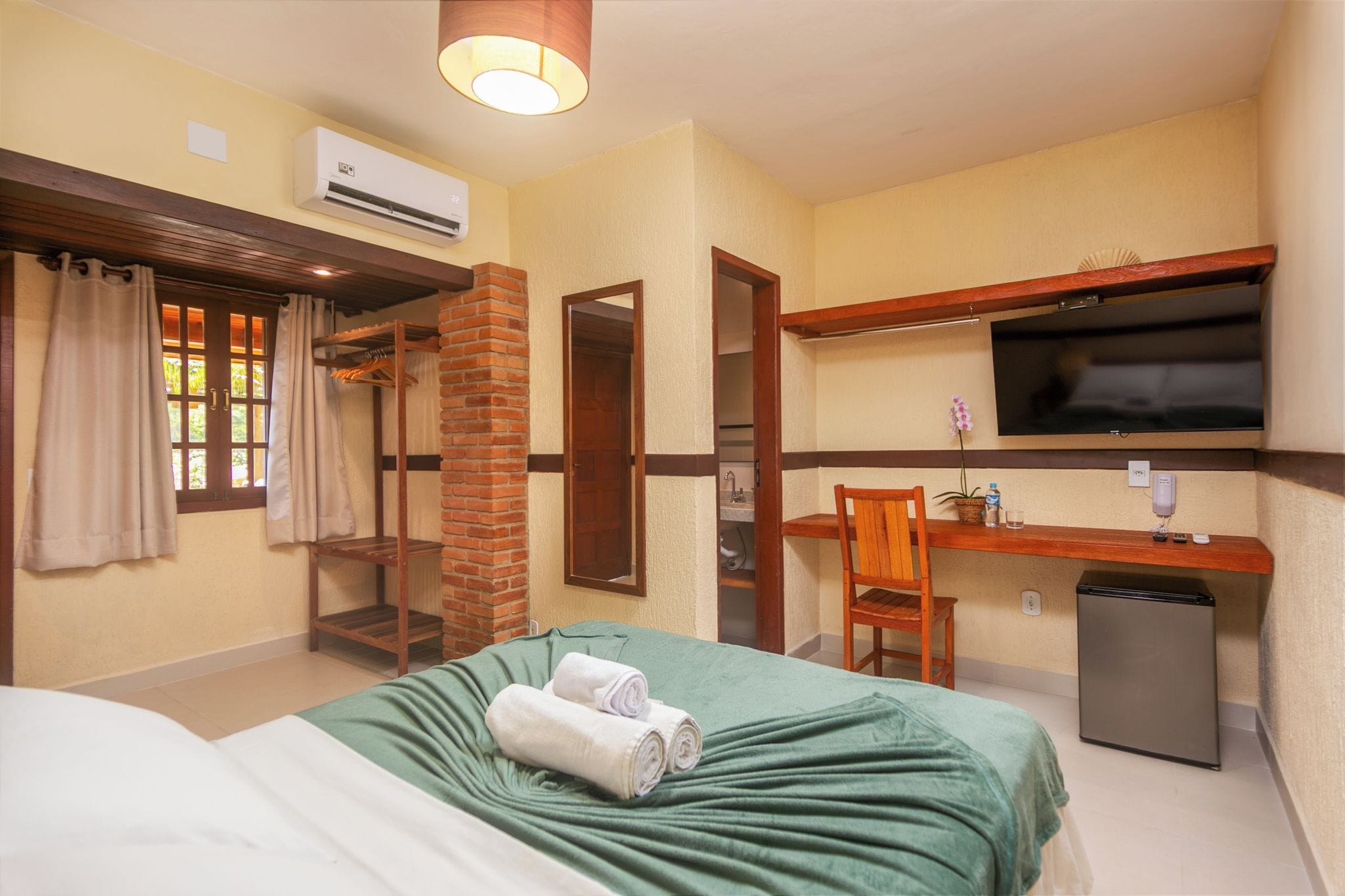 Quarto de hotel com cama, escrivaninha, televisão e pequeno frigorífico.