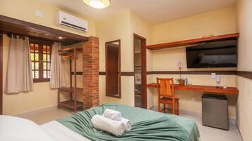 Quarto de hotel com cama, escrivaninha, televisão e pequeno frigorífico.