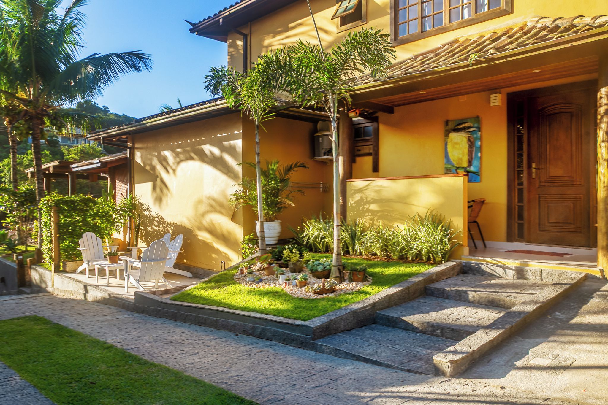 Una casa de dos pisos con un patio, mobiliario exterior y diversas plantas.