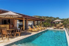 A poolside area with lounge chairs and umbrellas, a bar area, and a view of a mountainous landscape. - Pousada Búzios Garden (Búzios)