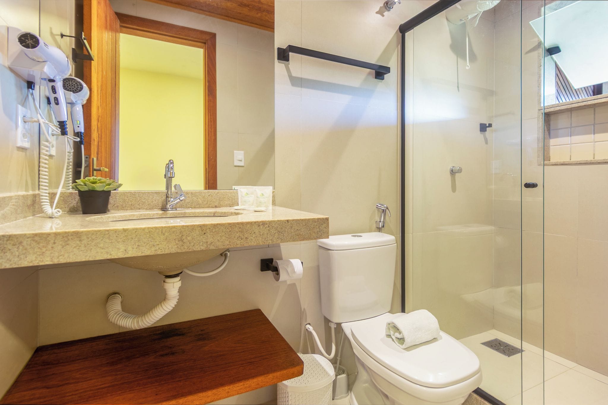 Un baño moderno con cabina de ducha de vidrio, inodoro y lavamanos con secador de pelo.