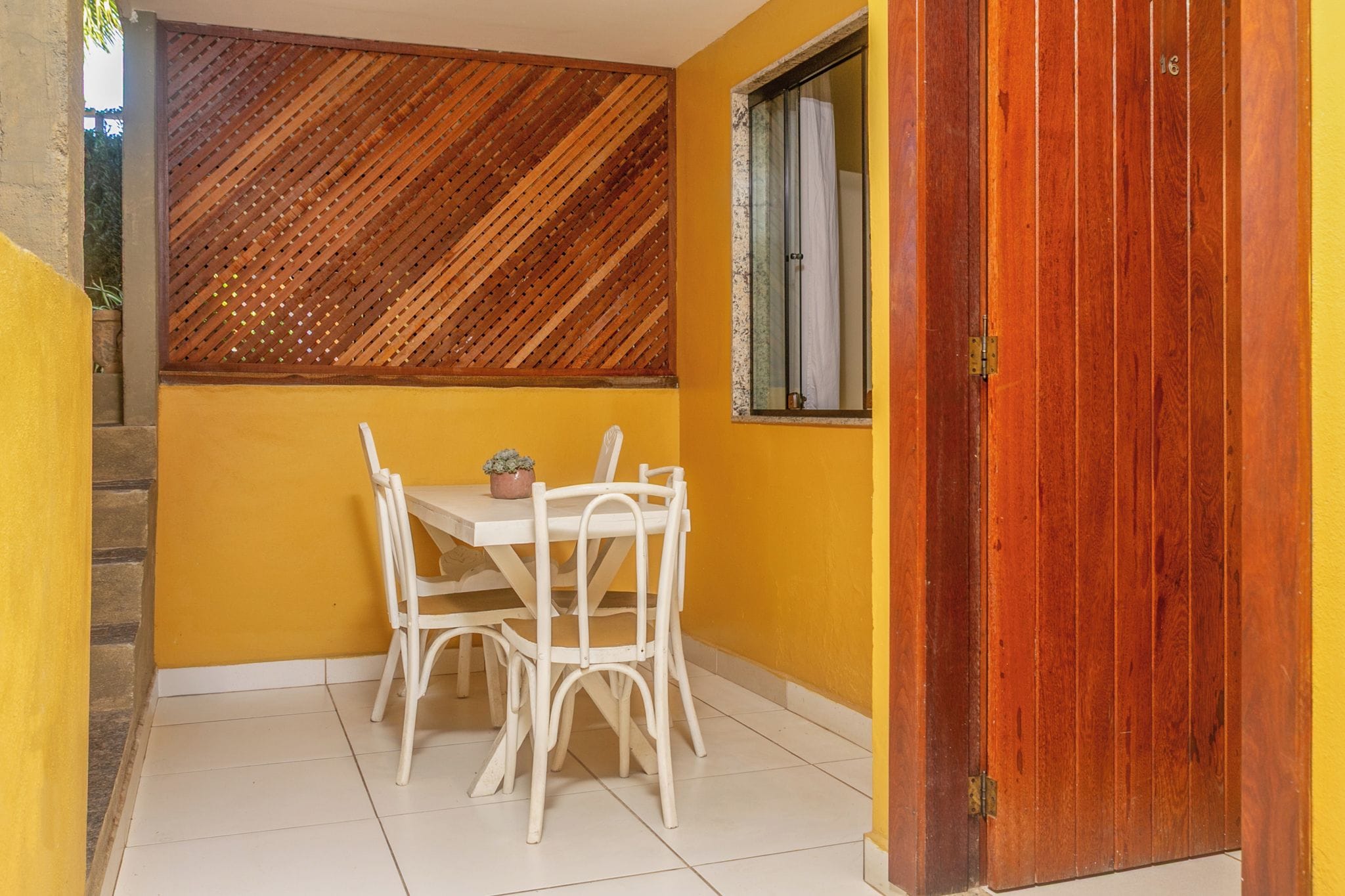 A small patio with a table and chairs, a wooden door, and a window with a curtain.